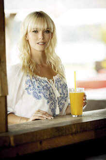 Porträt einer blonden Frau mit Getränk an einer Strandhütte - GDF01164