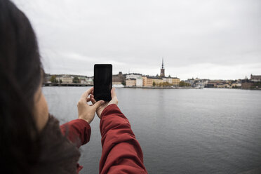 Schweden, Stockholm, Rückenansicht einer Frau, die ein Foto mit ihrem Smartphone von der Stadt aus macht - ABZF01437