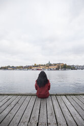Sweden, Stockholm, back view of woman sitting on pier looking to the city - ABZF01439