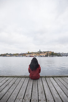 Schweden, Stockholm, Rückenansicht einer Frau, die auf einem Steg sitzt und auf die Stadt blickt - ABZF01439