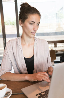 Junge Frau arbeitet mit Laptop in einem Café - TAMF00732