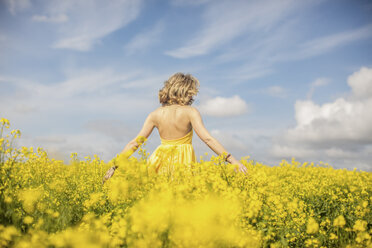 Back view of blond woman wearing yellow dress standing in rape field - ZEF11130