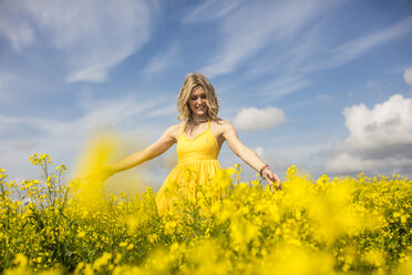 Happy blond woman wearing yellow dress standing in rape field - ZEF11131