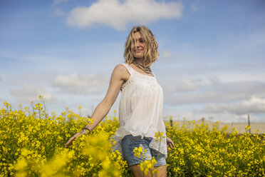 Smiling blond woman standing in rape field - ZEF11134