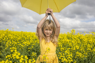 Portrait of blond little girl with yellow umbrella wearing yellow dress standing in rape field - ZEF11138