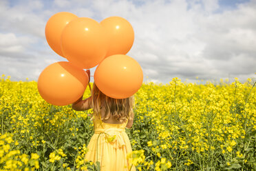 Rückenansicht eines kleinen Mädchens mit orangefarbenen Luftballons im Rapsfeld - ZEF11139