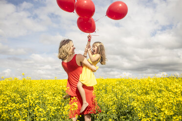 Mutter und kleine Tochter haben Spaß mit roten Luftballons im Rapsfeld - ZEF11140