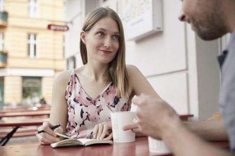 Lächelnde Frau mit Notizbuch, die einen Mann in einem Straßencafé ansieht, lizenzfreies Stockfoto