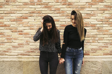 Two women holding hands in front of brick wall looking down - EBSF01851