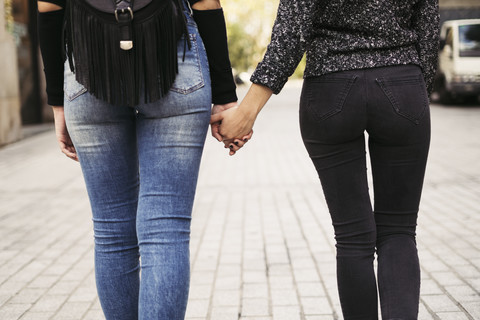 Rückenansicht von zwei Frauen, die sich auf der Straße an den Händen halten, lizenzfreies Stockfoto