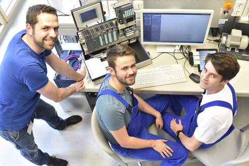 Portrait of smiling technical instructor with students at computer screen - LYF00636