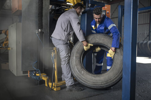 Zwei Reifenreparateure heben Reifen in einer Fabrik - ZEF11149