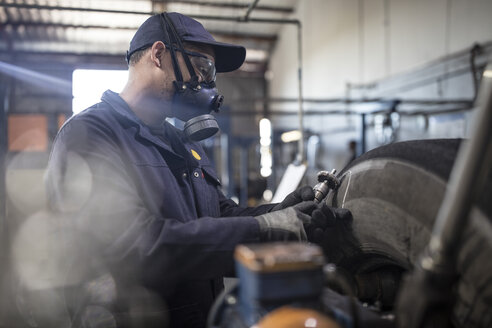 Reifenreparateur mit Maske schneidet Reifen mit einer Laufflächenschneidemaschine - ZEF11170