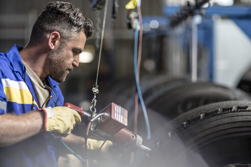 Reparateur bei der Arbeit an einem Reifen in einer Fabrik - ZEF11182