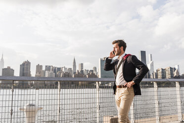 USA, New York City, businessman at East River on cell phone - UUF08845