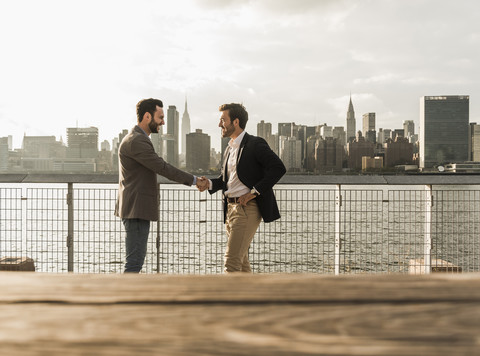 USA, New York City, zwei Geschäftsleute schütteln sich am East River die Hände, lizenzfreies Stockfoto