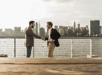 USA, New York City, two businessmen shaking hands at East River - UUF08866