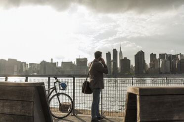 USA, New York City, businessman at East River on cell phone - UUF08873