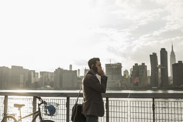 USA, New York City, businessman at East River on cell phone - UUF08874