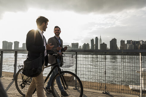 USA, New York City, zwei Geschäftsleute mit Fahrrad gehen am East River entlang - UUF08876