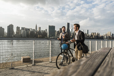 USA, New York City, zwei Geschäftsleute mit Fahrrad gehen am East River entlang - UUF08877