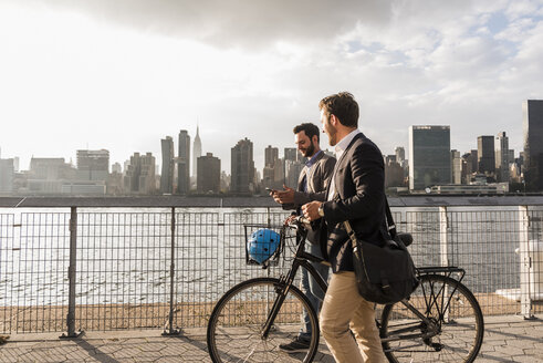 USA, New York City, zwei Geschäftsleute mit Fahrrad gehen am East River entlang - UUF08878