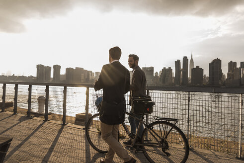 USA, New York City, zwei Geschäftsleute mit Fahrrad gehen am East River entlang - UUF08879