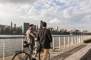 USA, New York City, zwei Geschäftsleute mit Fahrrad gehen am East River entlang - UUF08880