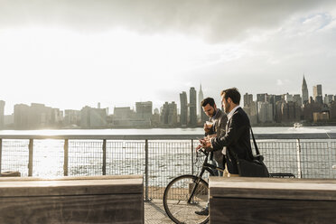 USA, New York City, zwei Geschäftsleute mit Fahrrad gehen am East River entlang - UUF08882