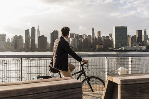 USA, New York City, Geschäftsmann auf Fahrrad mit Blick auf die Skyline von Manhattan - UUF08883