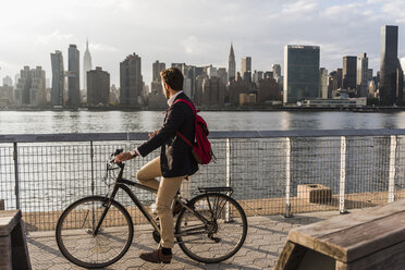 USA, New York City, Geschäftsmann auf Fahrrad mit Blick auf die Skyline von Manhattan - UUF08884