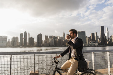 USA, New York City, businessman on bicycle with takeaway coffee - UUF08885