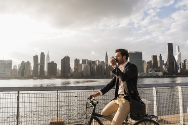 USA, New York City, Geschäftsmann auf Fahrrad mit Kaffee zum Mitnehmen - UUF08885
