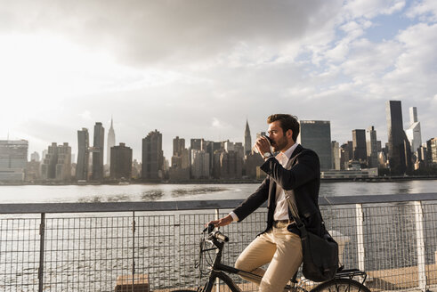 USA, New York City, Geschäftsmann auf Fahrrad mit Kaffee zum Mitnehmen - UUF08885