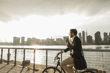 USA, New York City, businessman on bicycle with takeaway coffee - UUF08886