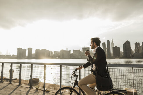 USA, New York City, Geschäftsmann auf Fahrrad mit Kaffee zum Mitnehmen - UUF08886