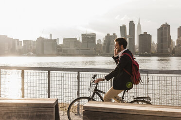 USA, New York City, Geschäftsmann auf Fahrrad, der mit einem Handy telefoniert - UUF08888