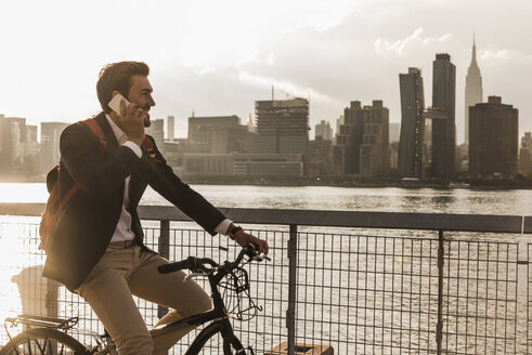 USA, New York City, Geschäftsmann auf Fahrrad, der mit einem Handy telefoniert - UUF08889