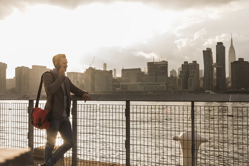 USA, New York City, Geschäftsmann am East River mit Mobiltelefon - UUF08891