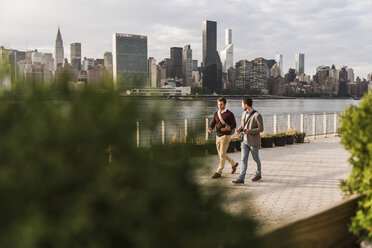 USA, New York City, zwei junge Männer gehen am East River entlang - UUF08905