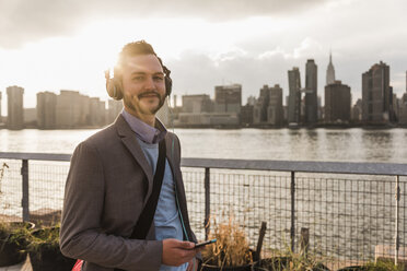 USA, New York City, portrait of smiling young man with headphones and cell phone - UUF08910