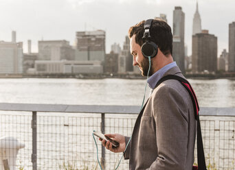 USA, New York City, junger Mann mit Kopfhörern und Mobiltelefon am East River - UUF08911