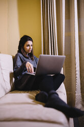 Junge Frau sitzt auf der Couch und benutzt einen Laptop - JRFF00988
