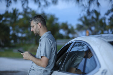 Junges Paar fährt Auto, Beifahrer benutzt Smartphone, lizenzfreies Stockfoto