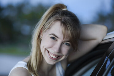 Smiling woman leaning against car, portrait - SHKF00706