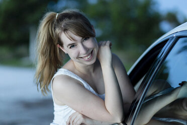 Smiling woman leaning against car, portrait - SHKF00707