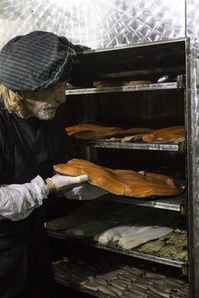Mann betrachtet ein frisch geräuchertes Lachssteak in einer Räucherkammer - ABZF01461