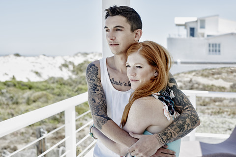 Glückliches junges Paar auf einer Terrasse eines Strandhauses mit Blick auf das Meer, lizenzfreies Stockfoto