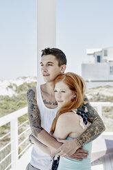 Glückliches junges Paar auf einer Terrasse eines Strandhauses mit Blick auf das Meer - RORF00369