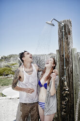 Junges Paar beim Duschen am Strand mit Kleidung - RORF00378